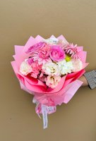 Hand-tied bouquet with pink ranunculus, pink gerberas, and white lisianthus wrapped in coordinating pink paper against a neutral background