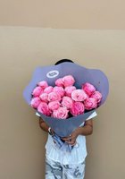 Person holding a large bouquet of 22 pink roses wrapped in purple paper against a neutral beige background