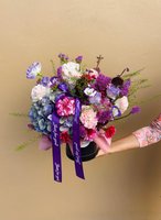 A lush purple flower box featuring hydrangeas, lisianthus, carnations, and chrysanthemums with decorative ribbons.