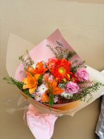 Bouquet of orange lilies and gerberas with pink roses, lavender blooms, and green fillers, wrapped in pink and beige paper.