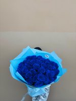 Hand-tied bouquet of 35 deep royal blue roses wrapped in light blue tissue paper against neutral background