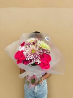 Person holding Yasmine bouquet with bright magenta roses and white chrysanthemums with green and purple tips, wrapped in white tissue paper
