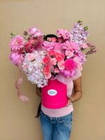 Person holding luxury pink box arrangement with pink gerberas, coral roses, lavender stock, pink carnations and white hydrangeas tied with pink rib...