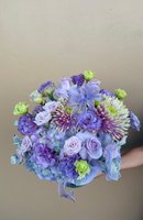Hand holding elegant purple and lavender bouquet with striped chrysanthemums, lisianthus, carnations and green roses tied with purple ribbon
