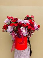 Elegant flower arrangement in red gift box featuring red roses and purple chrysanthemums with burgundy berries and ribbon, held by person in floral...