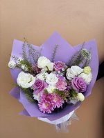 Bouquet of lavender roses, white lisianthus, and chrysanthemums wrapped in lilac paper.