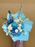 Blue and white flower bouquet with hydrangeas, chrysanthemums, lisianthus, and baby’s breath wrapped in pastel blue paper.