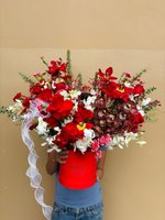 Person holding red hat box containing luxury flower arrangement with red lilies, red and white roses, burgundy orchids, and red carnations with whi...