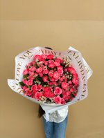Large bouquet of fuchsia spray roses, carnations, and white fillers wrapped in white paper with gold print.