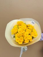 Bouquet of eighteen bright golden yellow roses wrapped in cream paper, held against a neutral beige background