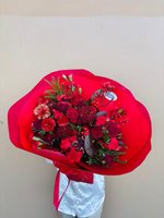 Elegant hand-tied bouquet with burgundy roses, red carnations, and burgundy chrysanthemums wrapped in bright red paper, featuring evergreen sprigs...